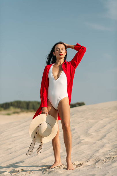 A young beautiful girl with a good figure, around only white sand and blue sky, and on her a white swimsuit and beautiful accessories - 写真・画像