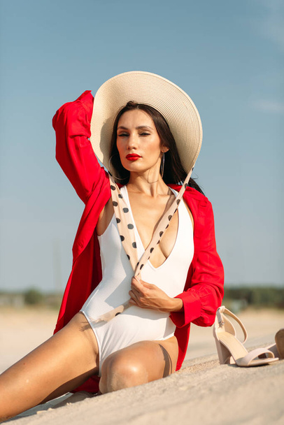 A young beautiful girl with a good figure, around only white sand and blue sky, and on her a white swimsuit and beautiful accessories - Foto, afbeelding