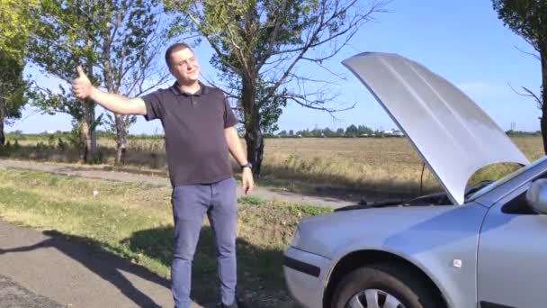 An angry man votes on the road. The driver stands near his car with the hood open and asks for help. Passing cars don't stop. Roadside Assistance Concept - Footage, Video
