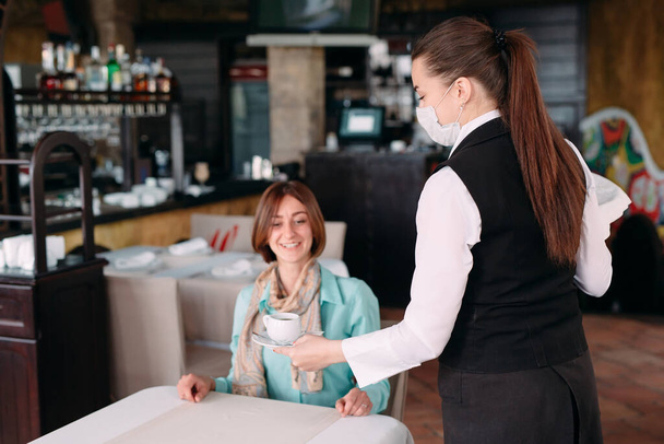 A European-looking waiter in a medical mask serves coffee. - Zdjęcie, obraz
