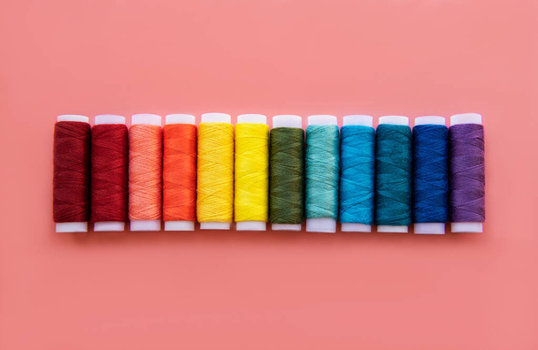 Spools of thread on the colors of the rainbow on a pink background, flat lay - Photo, Image
