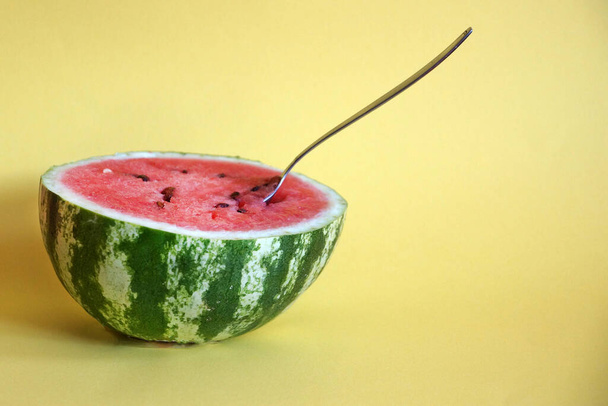 half watermelon with a spoon on a yellow background, copy space - Fotó, kép