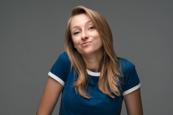 Studio shot of Good-looking woman with blonde straight hair wears blue t shirt, looks away enigmatically, wanting to do something illegally or secretly - Photo, Image