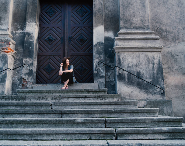 Portrét mladé krásné ženy v klobouku sedící na schodech středověké katedrály, cestující do Evropy - Fotografie, Obrázek