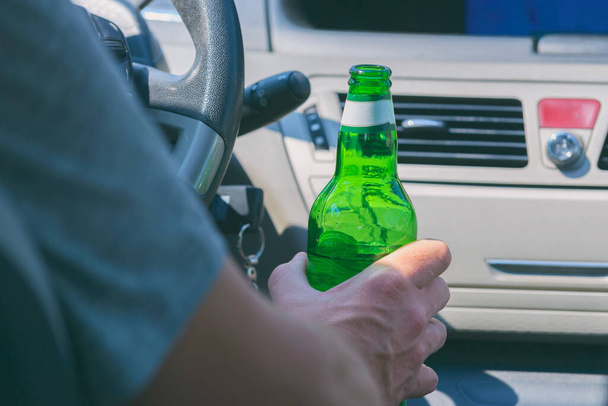 Άντρας κρατώντας πράσινο μπουκάλι μπύρας στο χέρι, ενώ οδηγείτε ένα αυτοκίνητο. Μην πίνετε και οδηγείτε. - Φωτογραφία, εικόνα
