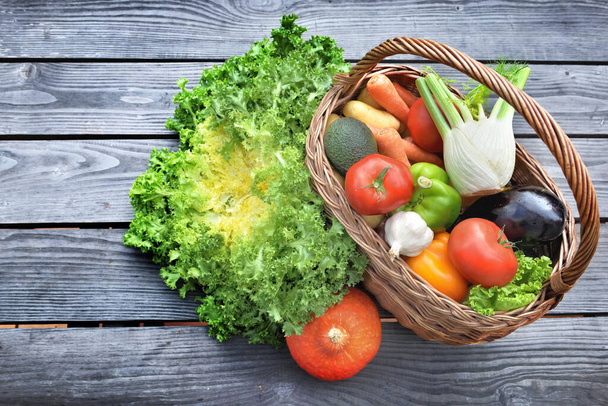 various and colorful vegetables in a wicker basket put on a wooden  table  - Foto, Imagen