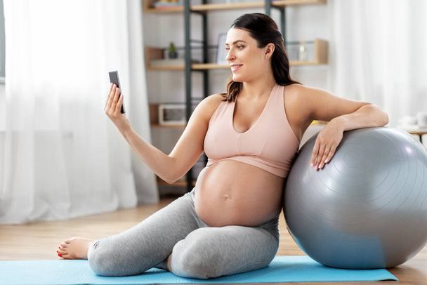 pregnant woman with phone and fitness ball at home - Photo, Image