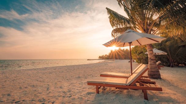 Beautiful tropical sunset scenery, two sun beds, loungers, umbrella under palm tree. White sand, sea view with horizon, colorful twilight sky, calmness and relaxation. Inspirational beach resort hotel - Photo, Image