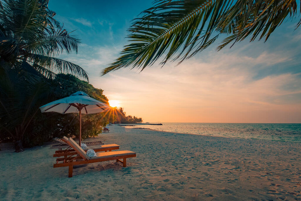 Beautiful tropical sunset scenery, two sun beds, loungers, umbrella under palm tree. White sand, sea view with horizon, colorful twilight sky, calmness and relaxation. Inspirational beach resort hotel - Photo, Image