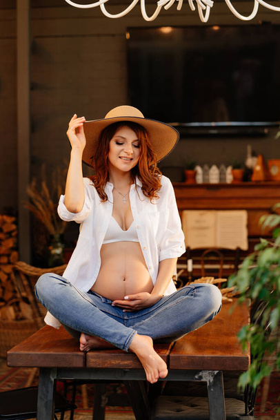 pregnant is sitting on table in country house. - Фото, изображение