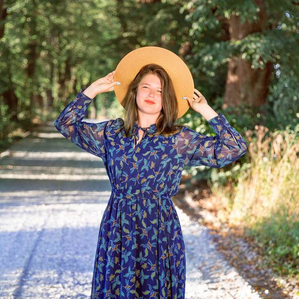 Ένα νεαρό κορίτσι με ένα μπλε μεταξωτό φόρεμα στέκεται στη φύση.  - Φωτογραφία, εικόνα