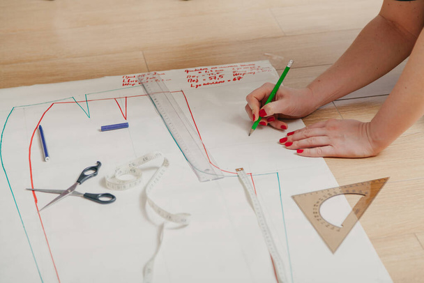Designer creates a model. Female hands with a manicure do the layout of the sewing pattern on pape - Foto, Bild