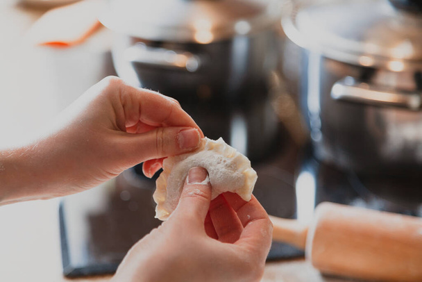 woman's hands are making a damp dumpling. In the background a metal saucepan and a wooden rolling pi - Fotografie, Obrázek