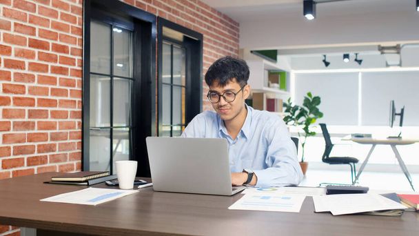 Молодой азиатский бизнесмен концентрируется на работе с ноутбуком в офисе, азиатский офисный работник comtemplate на работе с ноутбуками бизнес-людей и концепции офисного образа жизни - Фото, изображение