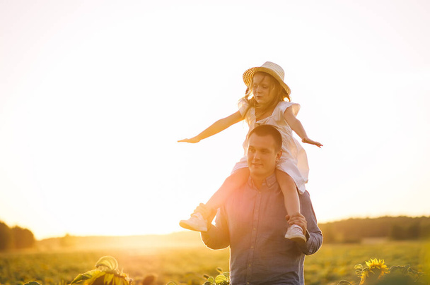 Ευτυχισμένος πατέρας και κόρη σε ψάθινο καπέλο διασκεδάζουν στον τομέα του ηλιοτρόπιου και παίζουν σε ένα παιχνίδι - αεροπλάνο. - Φωτογραφία, εικόνα