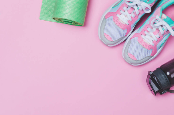 Mata do jogi, buty sportowe, butelka wody na różowym tle. Zdrowy styl życia - Zdjęcie, obraz