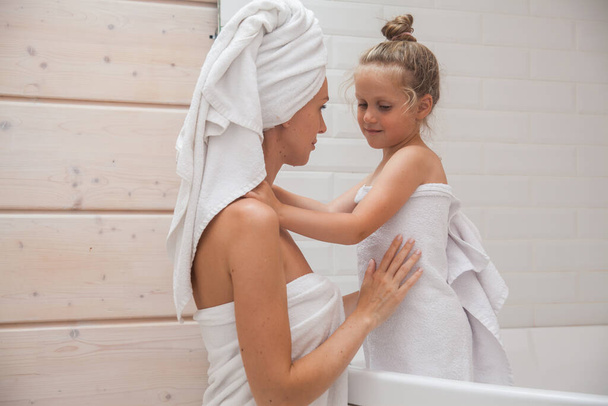 Happy loving family spending time together. Mother and her daughter child girl kissing and hugging in white bathroom. Woman and girl with towels on their heads and bodies  - Photo, Image