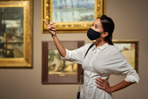 Mujer visitante con una máscara antivirus en el museo histórico mirando fotos. - Foto, imagen