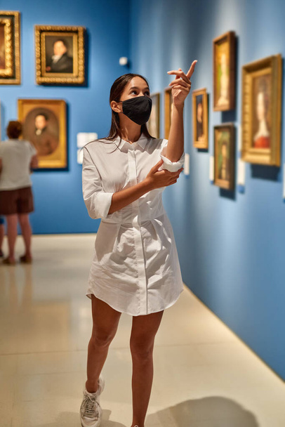 Woman visitor wearing an antivirus mask in the historical museum looking at pictures. - Photo, Image