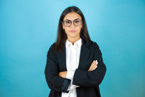 Young beautiful business woman over isolated blue background crossed arms looking at the camera very serious - Foto, afbeelding