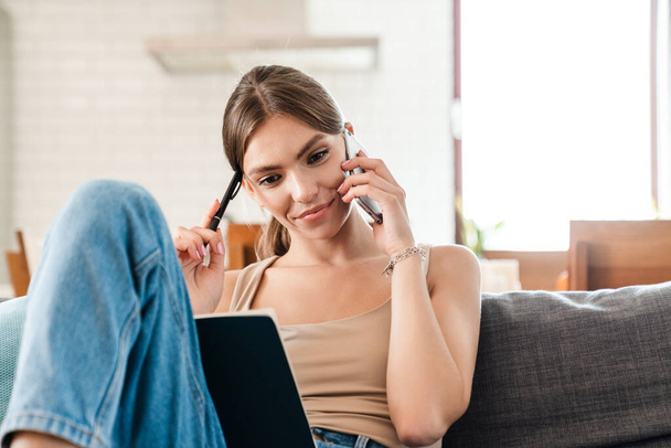 Casual young woman using laptop and cellphone on sofa at home - Foto, Bild