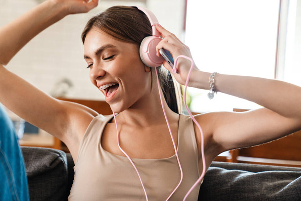 Attractive cheerful young woman listening to music with headphones, sitting on a couch - Foto, immagini