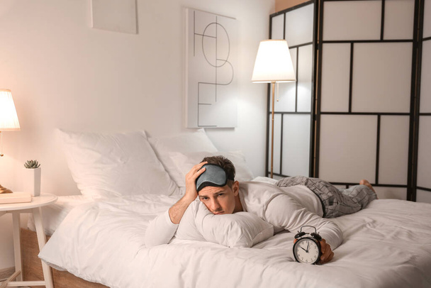 Hombre joven con despertador que sufre de insomnio en el dormitorio - Foto, imagen