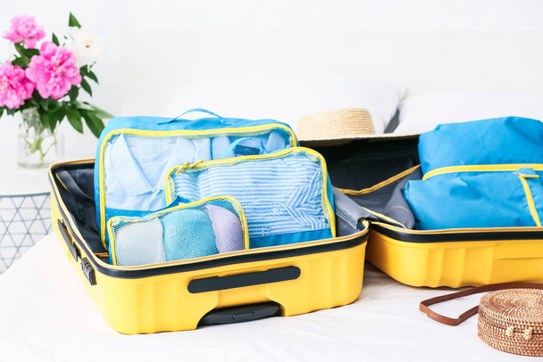 Koffer en set van reisorganisatoren met spullen op bed thuis - Foto, afbeelding