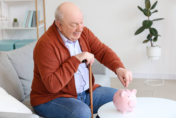 Vanhempi mies säästöpossun kanssa kotona - Valokuva, kuva