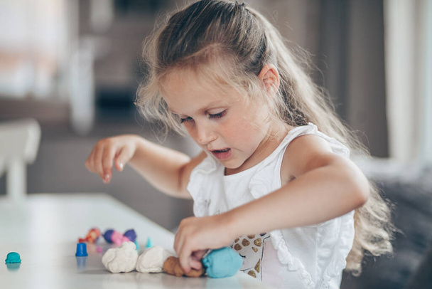 Little cute preschooler child girl playing educational games with plasticine figures preparing for school in kindergarten while sitting at table. Back to school concept - Photo, Image