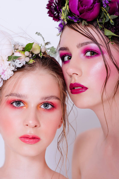 Bright and fashion spring art professional make-up for two beautiful sisters. Close up portrait. A hoop of fresh spring flowers peony on  heads. Model with clean skin, face care. Cosmetology for young - Valokuva, kuva