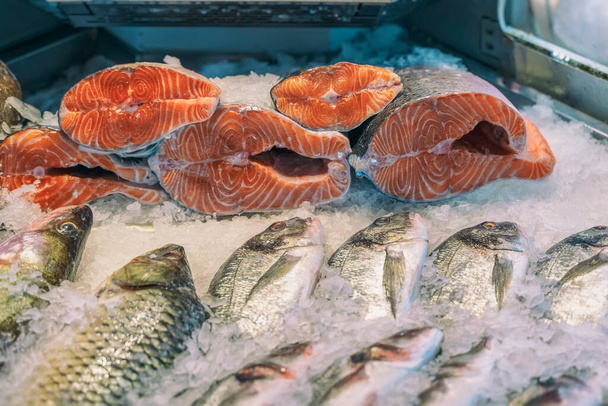Sale of fresh frozen fish on farmer's bazaar. Open showcases of seafood market. Fish store. Pieces of salmon fresh salmon on ice in supermarket close-up - Valokuva, kuva