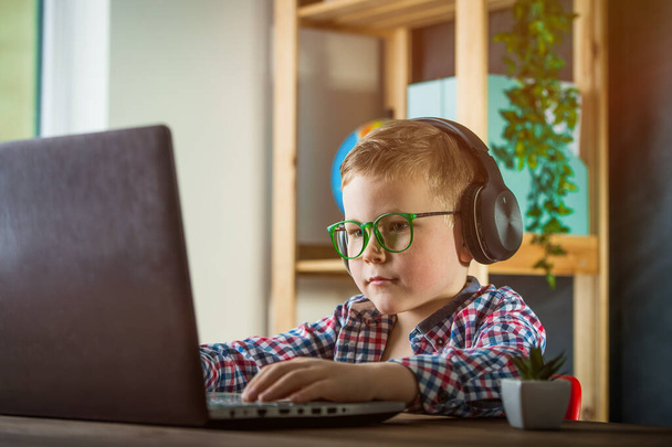 De vuelta a la escuela. Concepto de educación, tecnología y personas: niño con computadora y auriculares escribiendo en el teclado o jugando videojuegos en casa. - Foto, Imagen