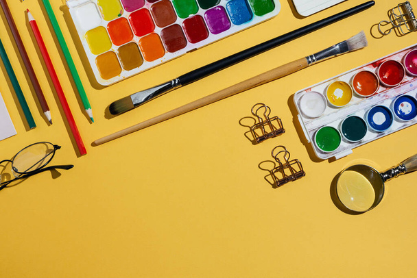 Flatlay of watercolors, brushes, notebooks and other stationery and art supplies on yellow - Foto, immagini