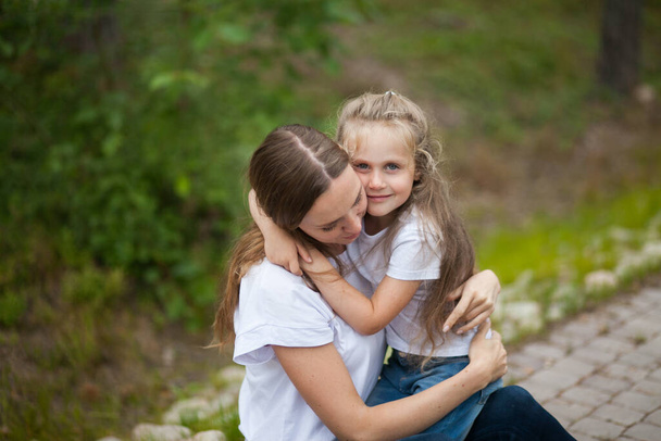Šťastná usměvavá matka a její roztomilé emocionální dceruška dítě v bílých košilích a džínách džíny se objímají a baví venku v přírodě na venkově. Trávit letní čas s rodinou - Fotografie, Obrázek