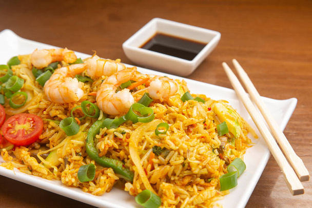 Chinesischer gebratener Reis mit Garnelen, auf hölzernem Hintergrund. Typisch asiatisches Essen. - Foto, Bild
