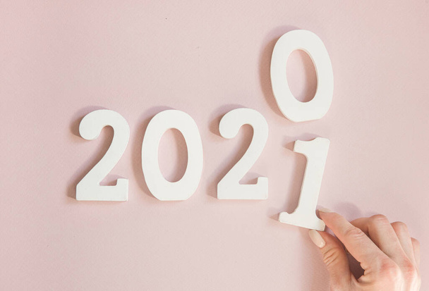 Primer plano de los números metálicos 2021 y mano sobre fondo naranja. año de cambio 2020 a 2021. - Foto, Imagen