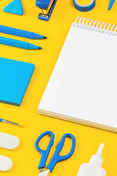 Assorted office and school white and blue stationery on bright yellow background. Organized knolling for back to school template or education and craft concept. Selective focus. Copy space - 写真・画像