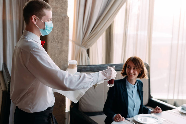 A European-looking waiter in a medical mask serves Latte coffee. - Photo, image