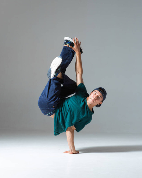 Cool b-boy dancing on one hand in studio isolated on gray background. Breakdance poster - Photo, Image