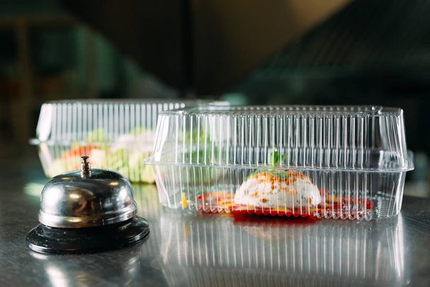 Yemek servisi. Metal çanı olan bir restoranda dağıtım masası. Plastik kaplarda yiyecek. Plastik konteynırlarda panna cotta ve sebze salatası.. - Fotoğraf, Görsel