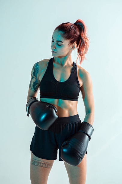 Beautiful female fighter in black boxing gloves posing in studio in neon light. Mixed martial arts poster - Фото, зображення