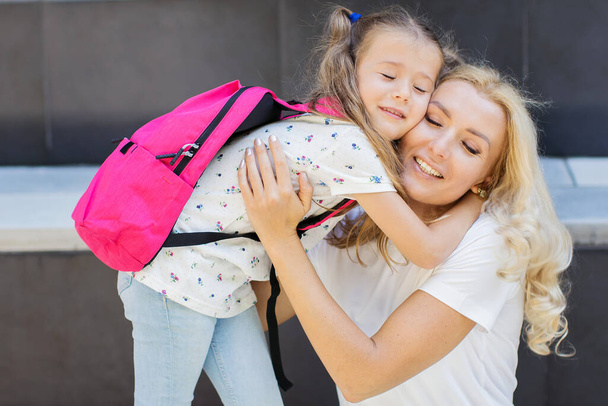 Little girl with the backpack hugging her mother at the first school day. - Photo, Image