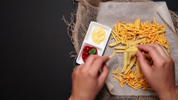 Az ember sült krumplit eszik ketchuppal és sajt szósszal egy sötét asztalon, felülnézetből. lapos fektetés - Felvétel, videó