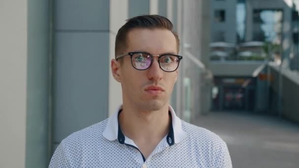 Portrait of shocked young businessman takes off his glasses in surprise. Astonished man scared by the news looks at the camera against the background of the citys business district - Footage, Video
