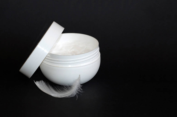 pot blanc ouvert de crème et de plume blanche sur fond noir, espace de copie - Photo, image