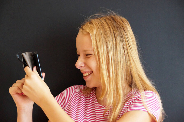 retrato de la muchacha adolescente riendo con el teléfono en el fondo negro. - Foto, imagen