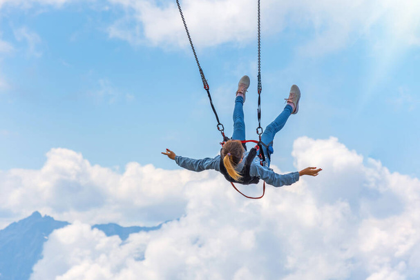 Fille balançant sur une balançoire suspendue au-dessus d'un abîme sur fond de montagnes et de ciel et de nuages - Photo, image