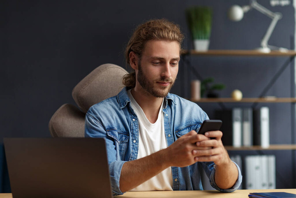 Young man using smartphone and smiling. Happy businessman using mobile phone apps, texting message, browsing internet, looking at smartphone. Concept of young people working with mobile devices - Foto, imagen