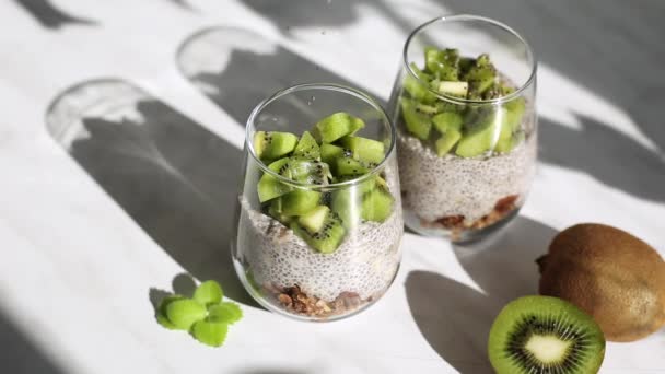 Chia-Pudding mit Kokosmilch und Kiwi im Glas mit Müsli. Gesunde vegane Ernährung. Sonnenlicht in der Küche aus dem Fenster, Blendung, Strahlen und leuchtende Früchte. - Filmmaterial, Video